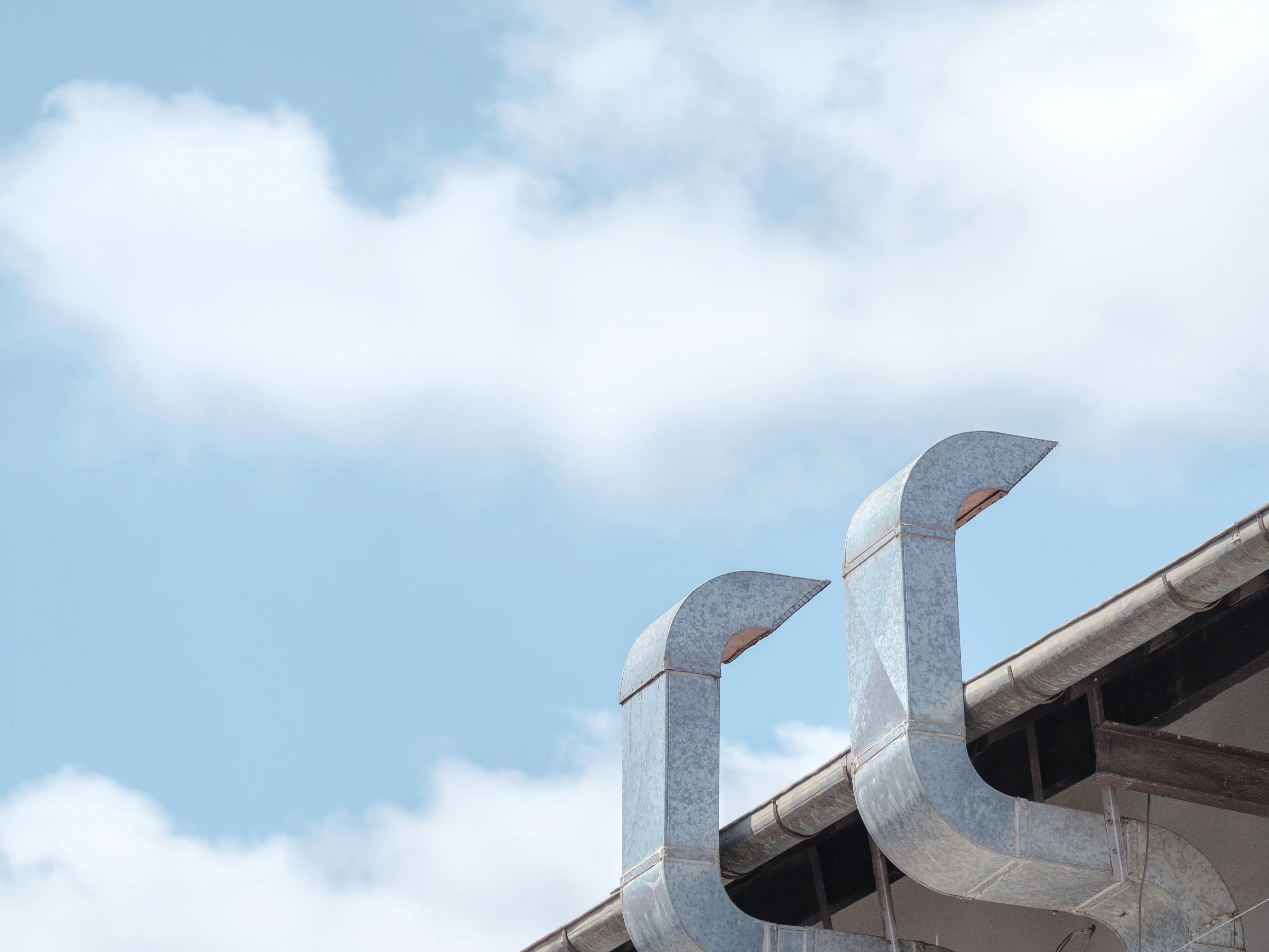 Ventilation ducts on a rooftop against a blue sky with clouds