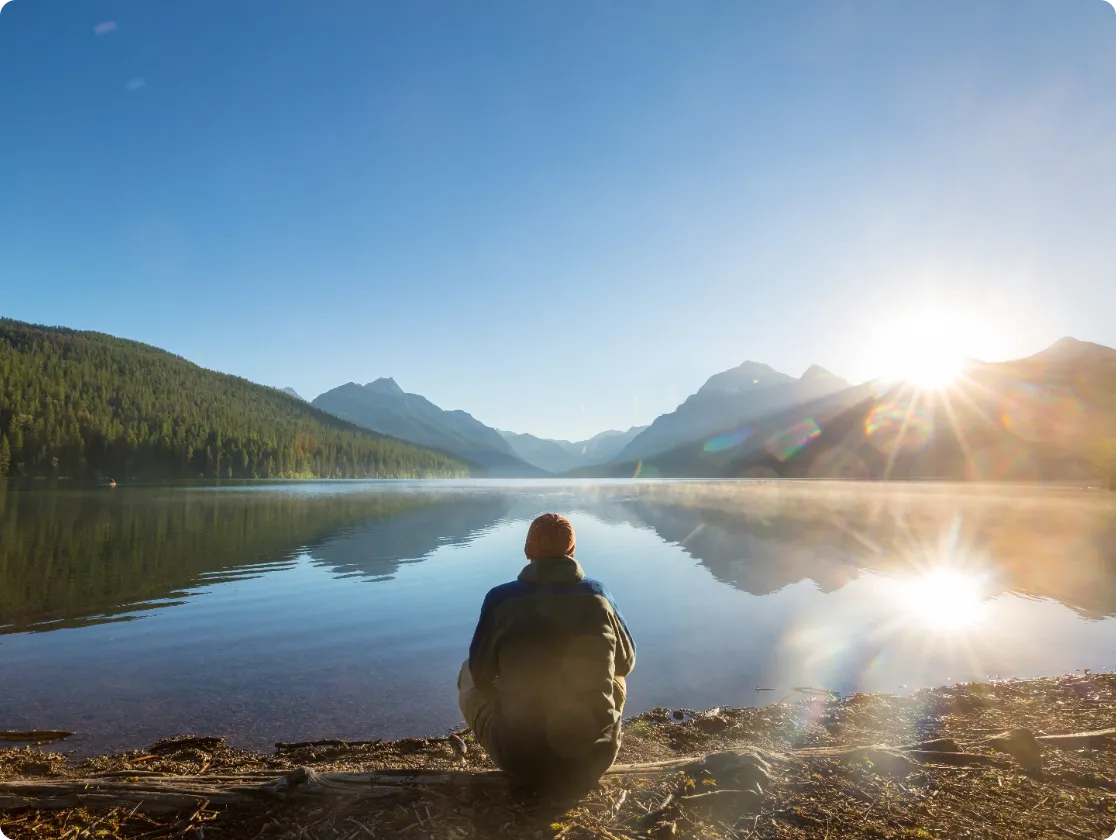 Person sitting by a calm mountain lake at sunrise