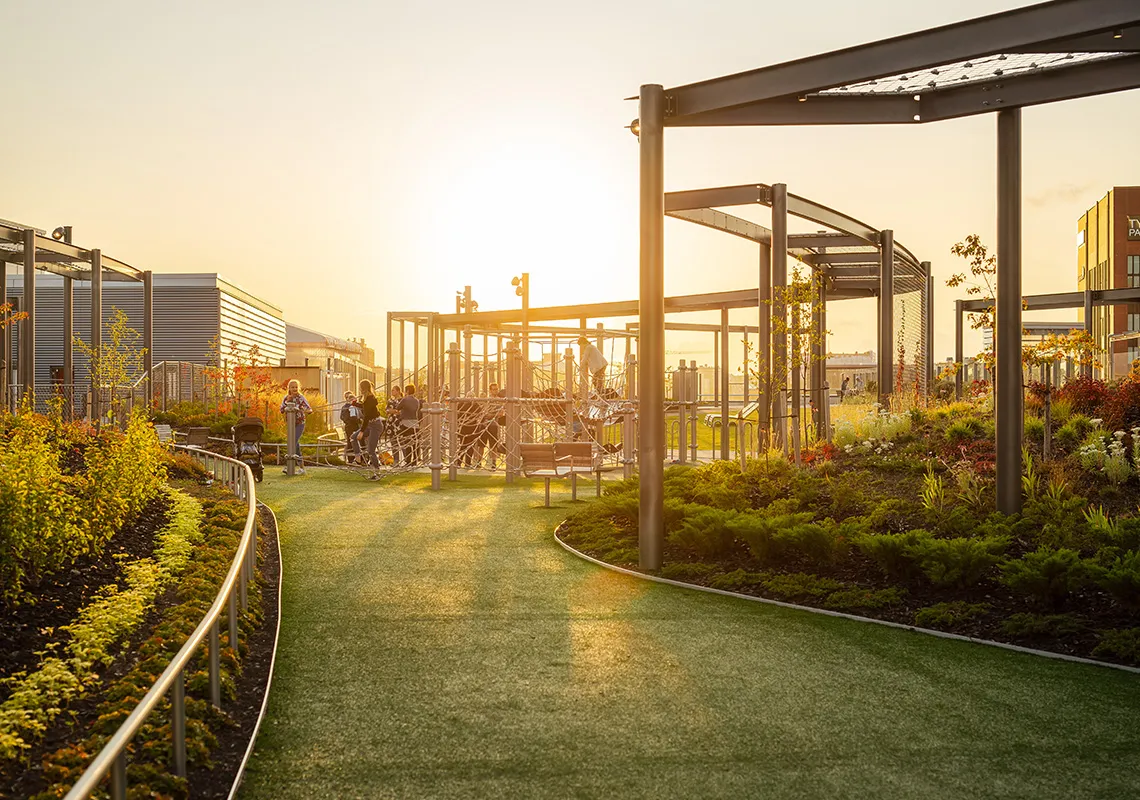 Modern urban park with playground structures and people enjoying the space at sunset.
