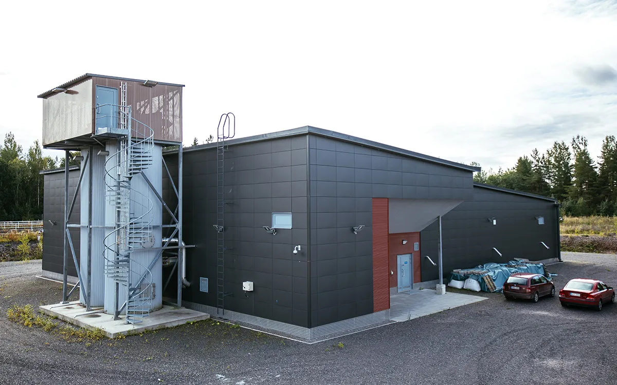 Extérieur du bâtiment de l’usine de traitement d’eau de Jäniksenlinna, avec des voituresstationnées à proximité et une zone boisée environnante