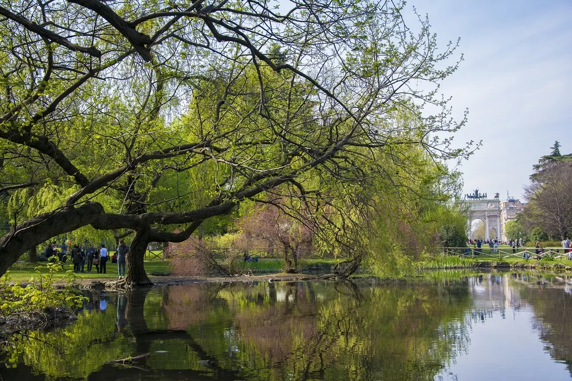 Vue du parc Sempione, au centre de Milan, avec sa végétation luxuriante, un étang réfléchissant etl’historique Arco della Pace en arrière-plan