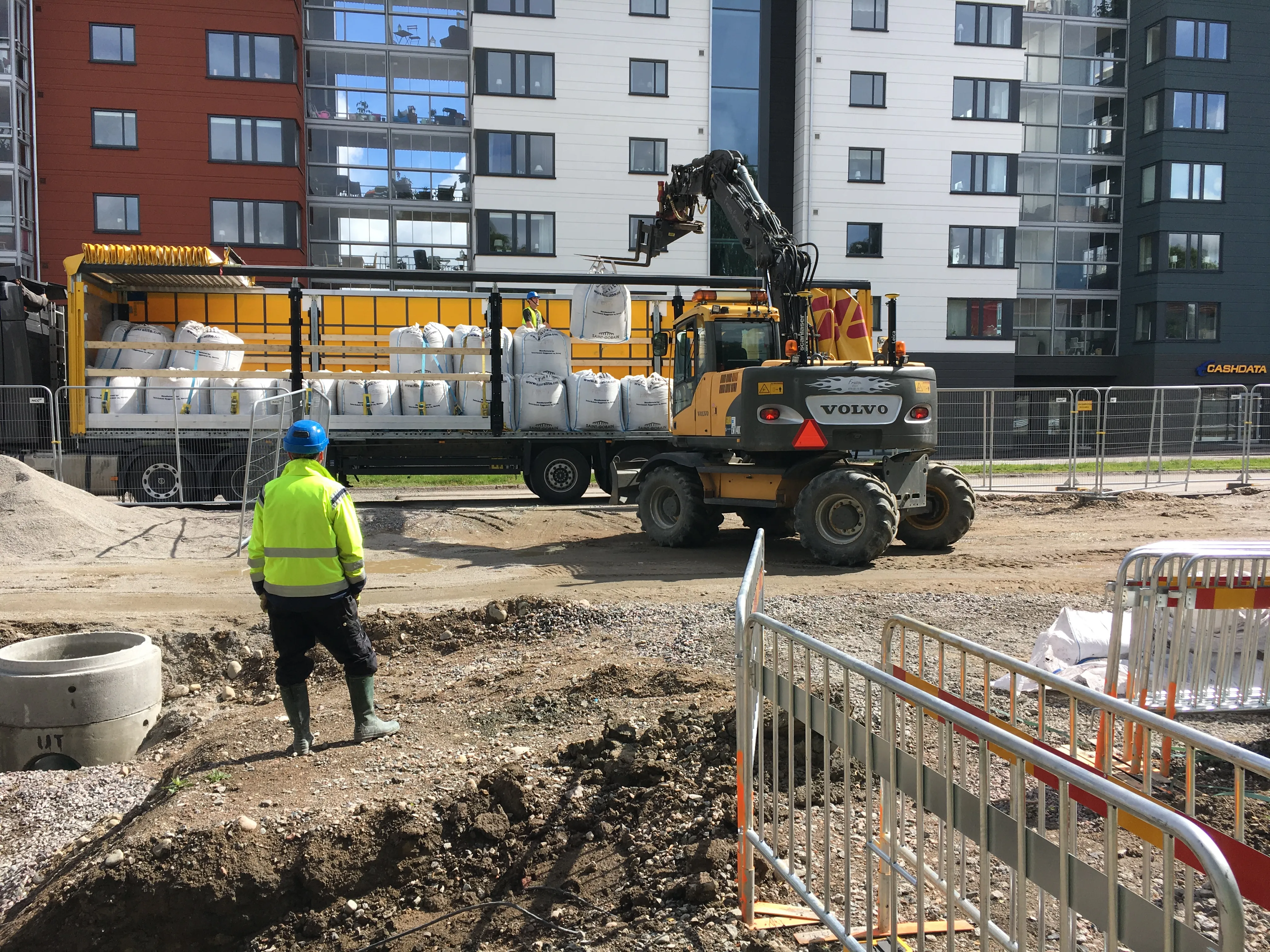 Construction site with an excavator unloading large bags of Filtralite filter media, supervised by a worker in safety gear