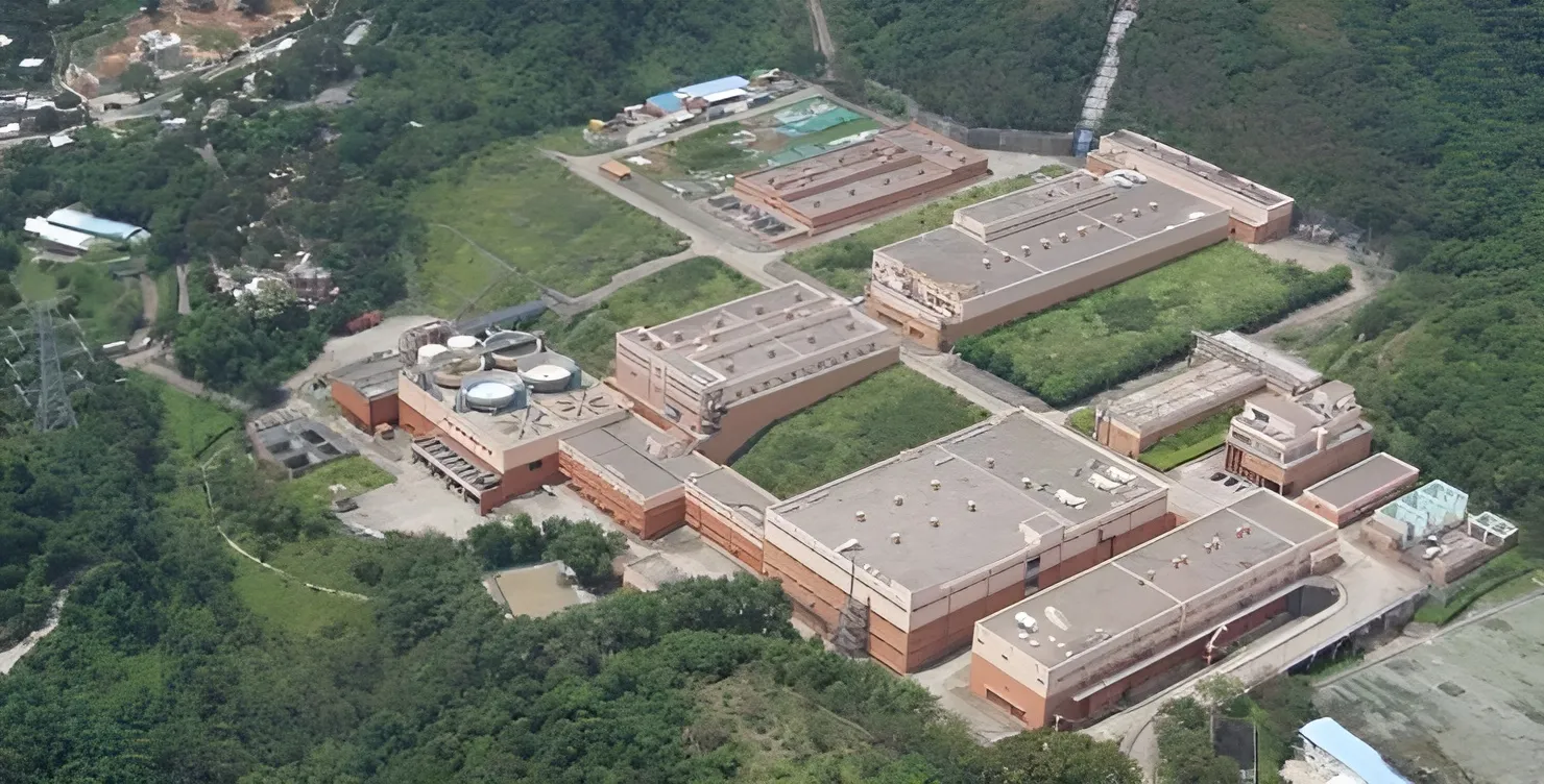Vue aérienne de la station de traitement d’eau de Tai Po à Hong Kong, montrant plusieurs grandsbâtiments de traitement entourés de collines verdoyantes