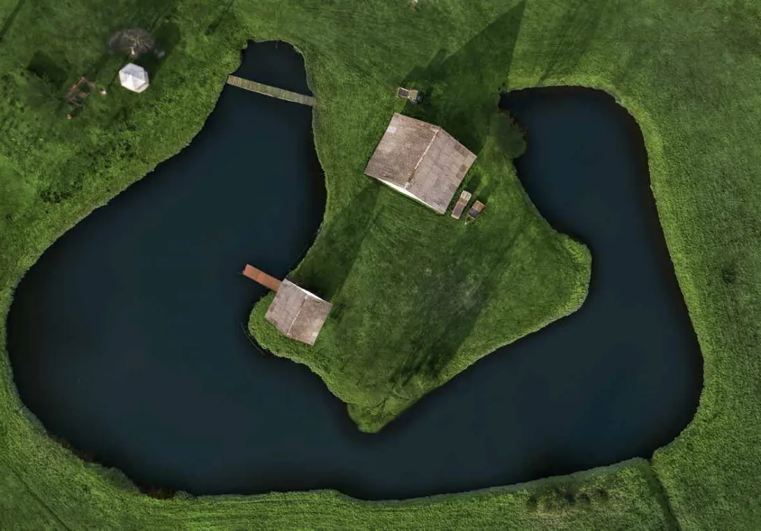 Aerial view of a small house on green land surrounded by a pond